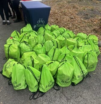 A large pile of bright green drawstring bags with the InTandem logo sitting on the ground next to a branded blue table.
